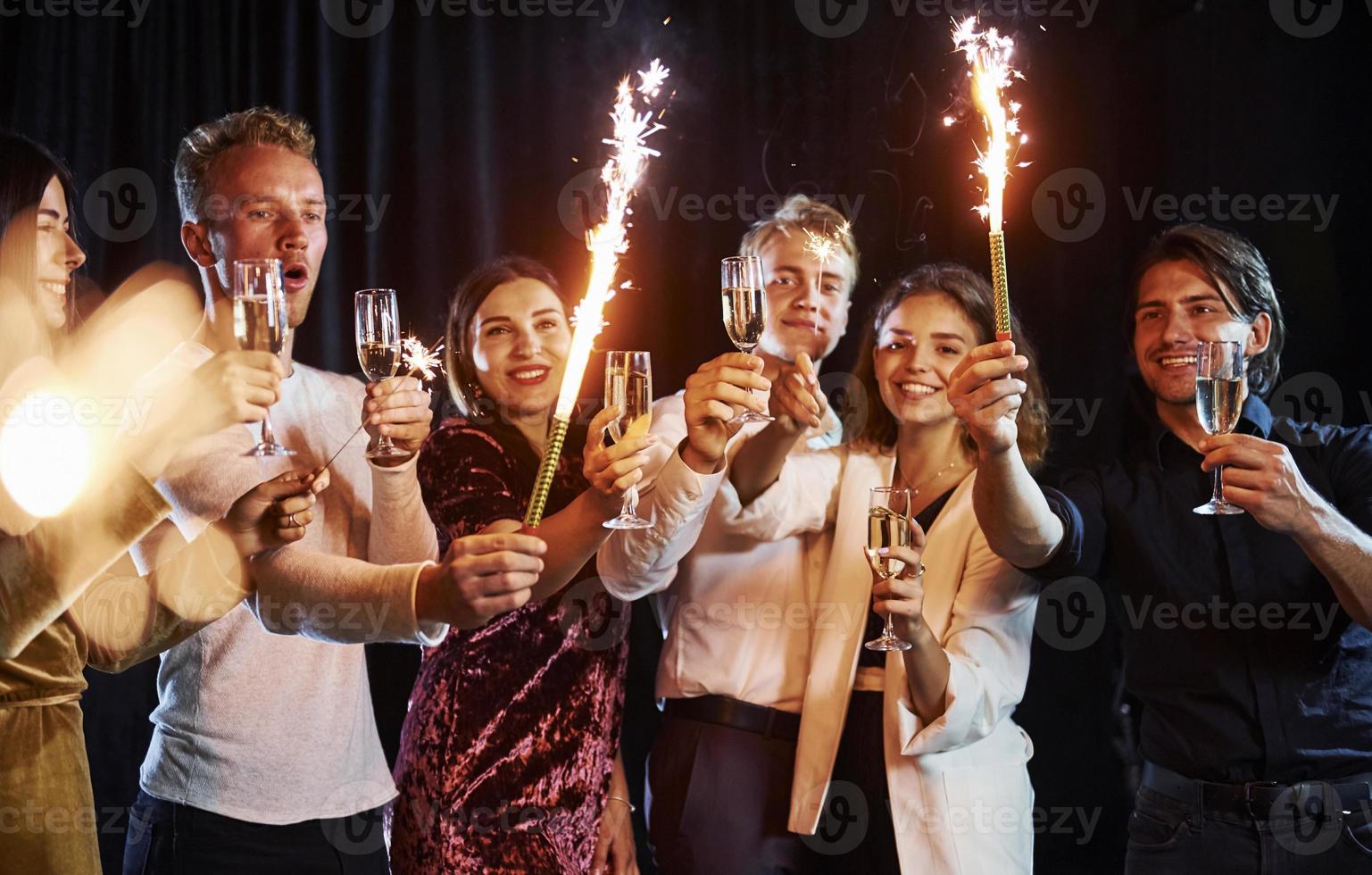 avendo divertimento con spumanti. gruppo di allegro amici festeggiare nuovo anno in casa con bevande nel mani foto
