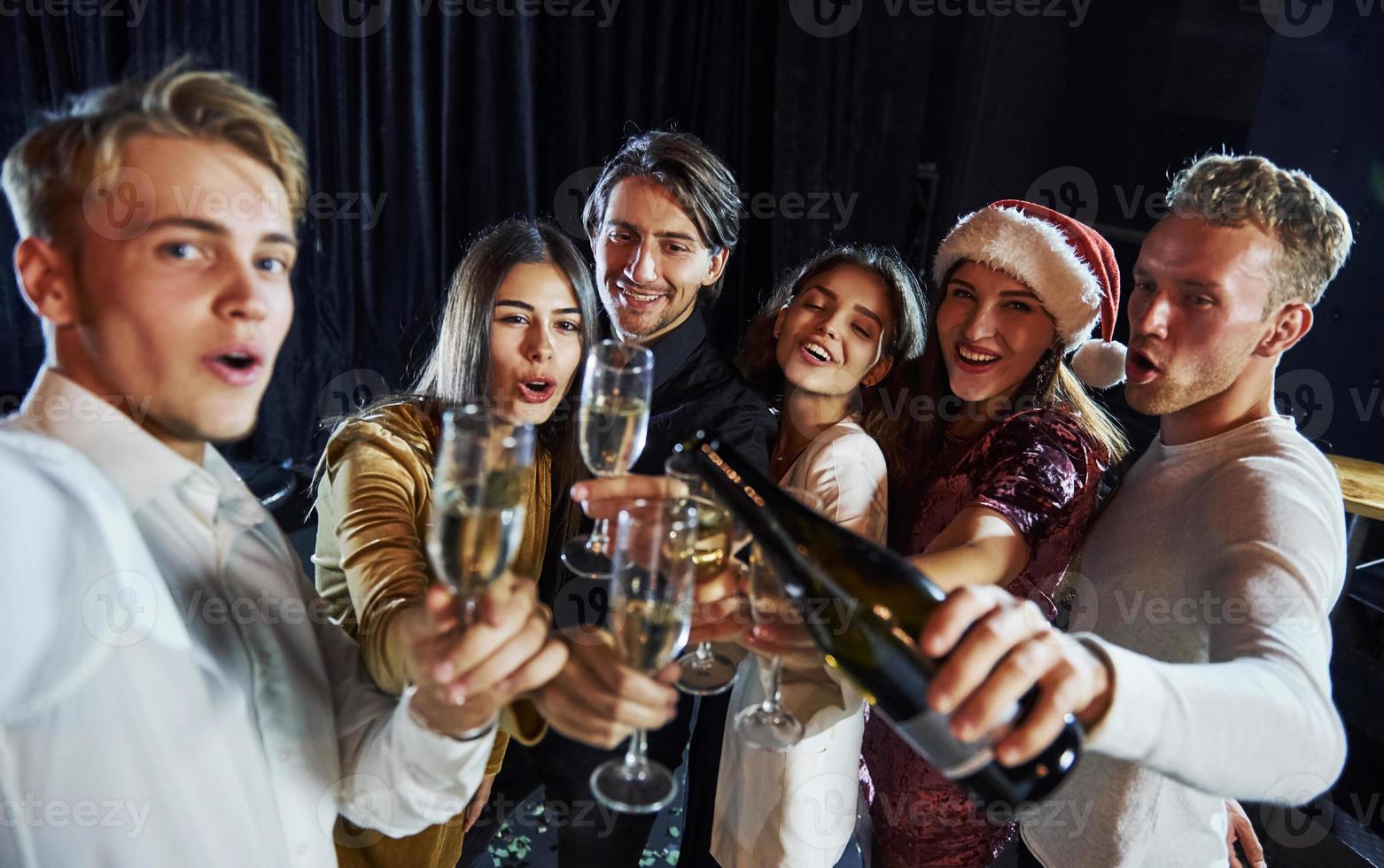 prende autoscatto. gruppo di allegro amici festeggiare nuovo anno in casa con bevande nel mani foto