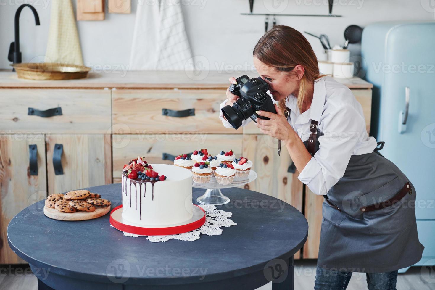 donna sta nel il cucina e prende foto di sua fatti in casa biscotti e torta di utilizzando telecamera