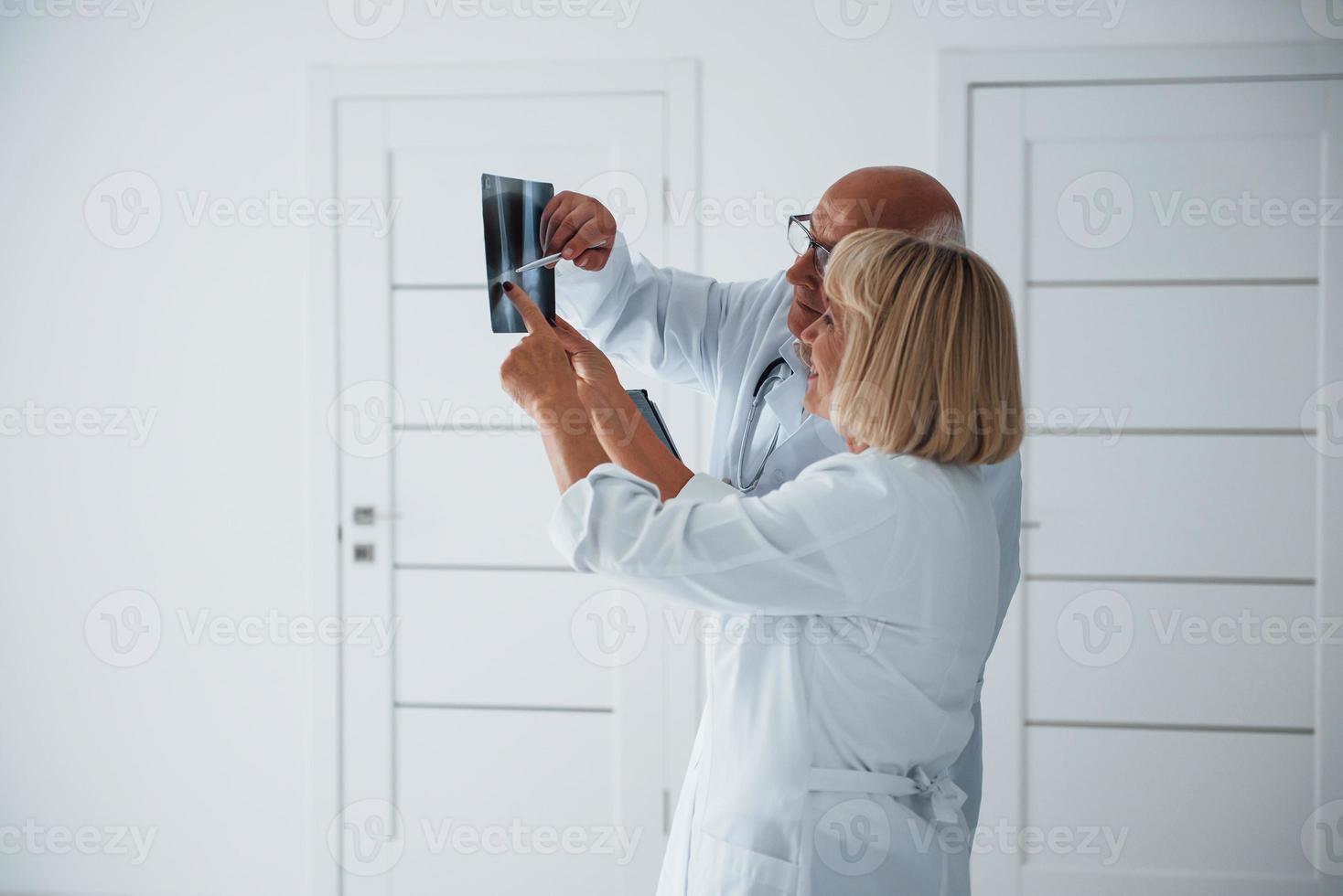 anziano uomo e donna medici nel bianca uniforme esamina raggi X di umano gambe foto