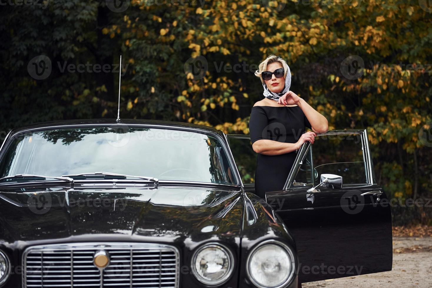 bionda donna nel occhiali da sole e nel nero vestito vicino vecchio Vintage ▾ classico auto foto