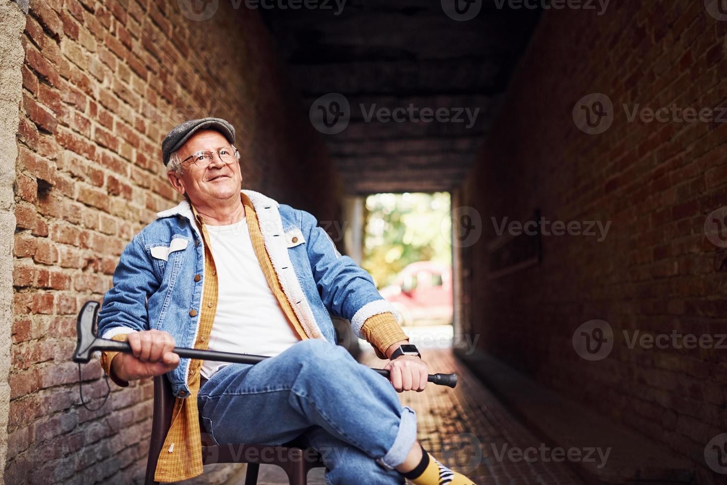 elegante anziano nel alla moda Abiti e nel bicchieri si siede su il sedia nel il città foto
