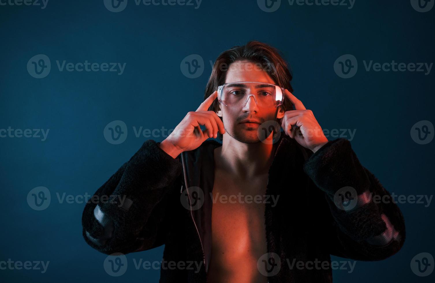 bellissimo lungo dai capelli caldo uomo nel bicchieri è nel il studio con blu neon illuminazione foto