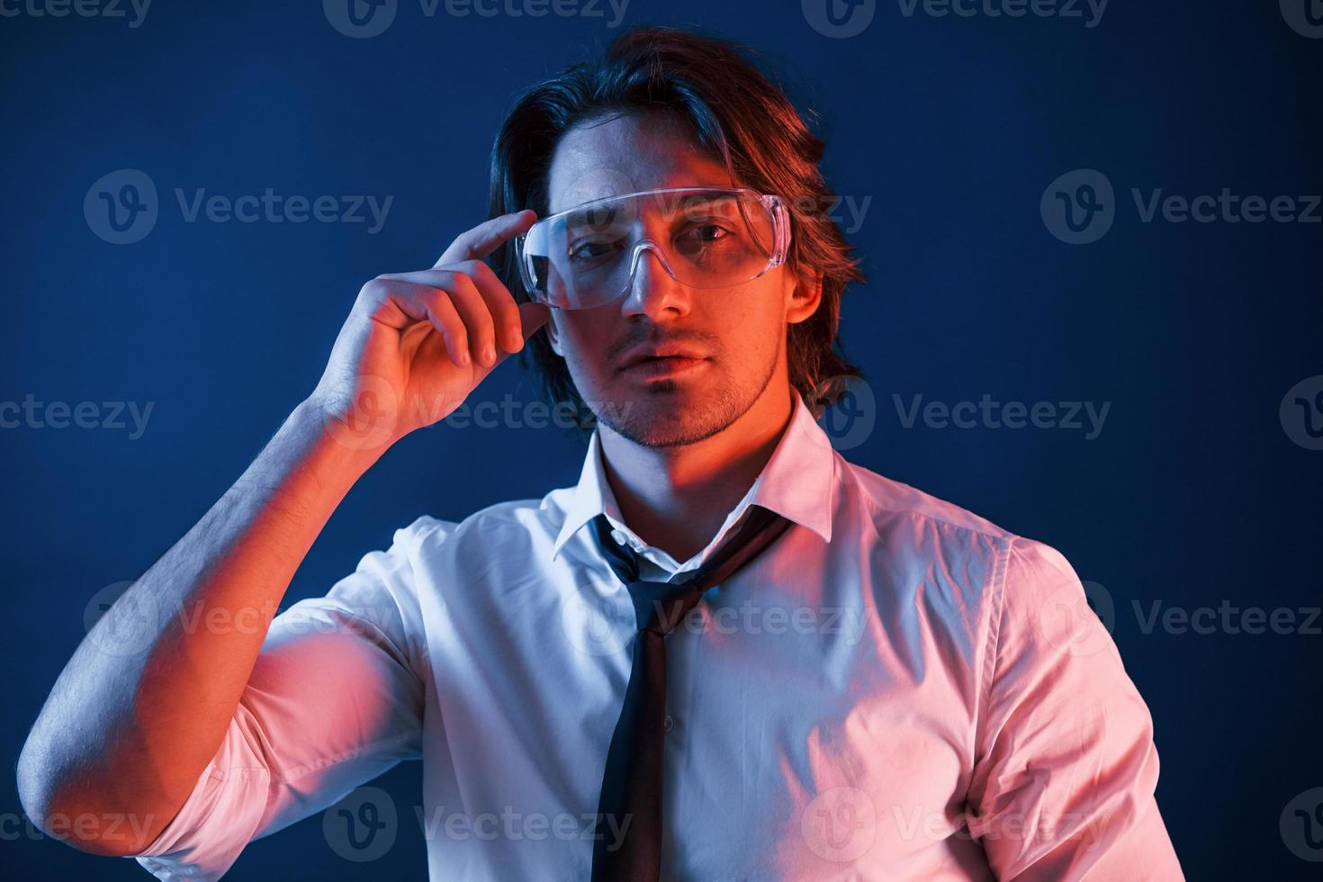 bellissimo uomo nel bicchieri e nel completo da uomo e cravatta è nel il studio con blu neon illuminazione foto