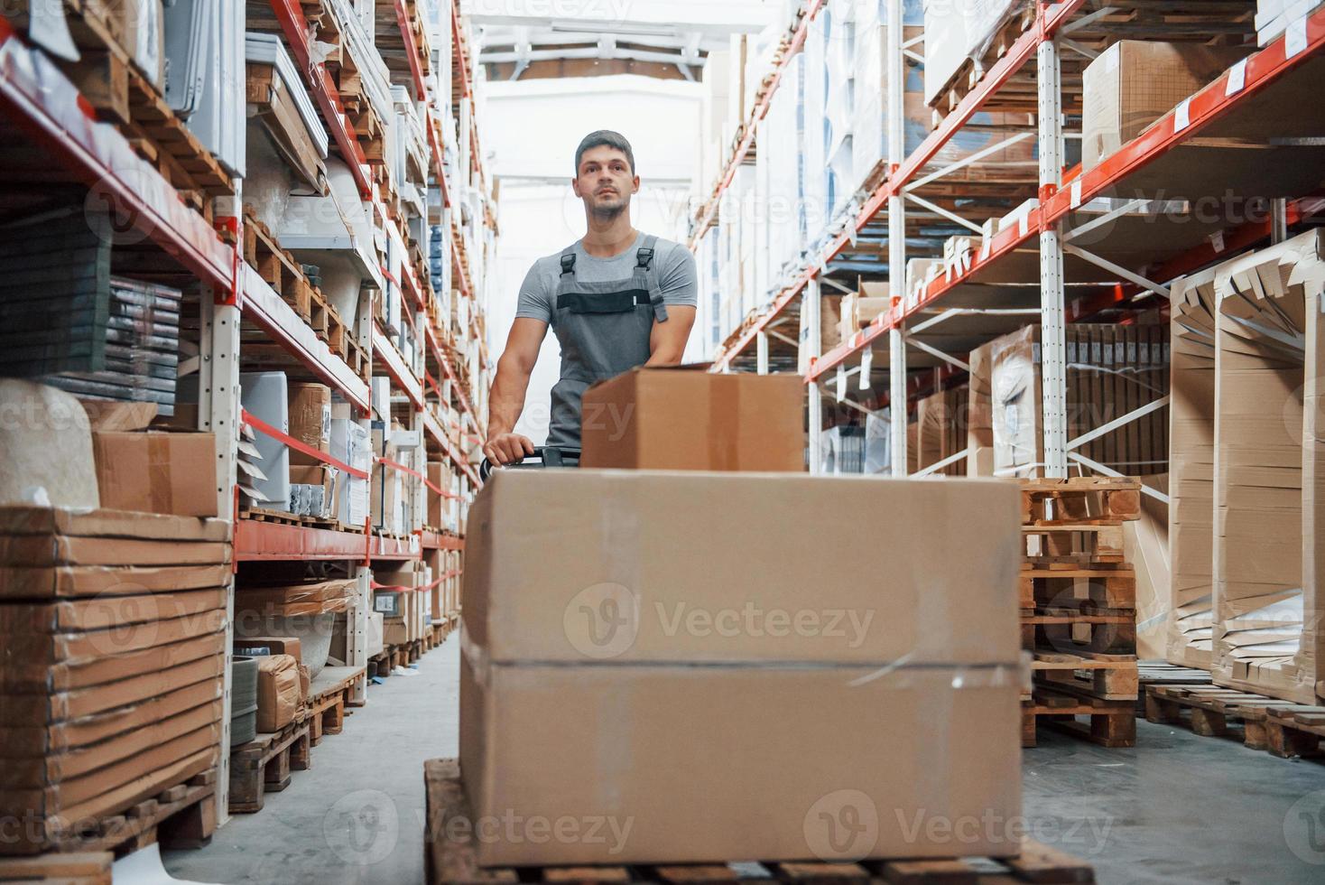 giovane maschio lavoratore nel uniforme è nel il magazzino spingendo pallet camion foto