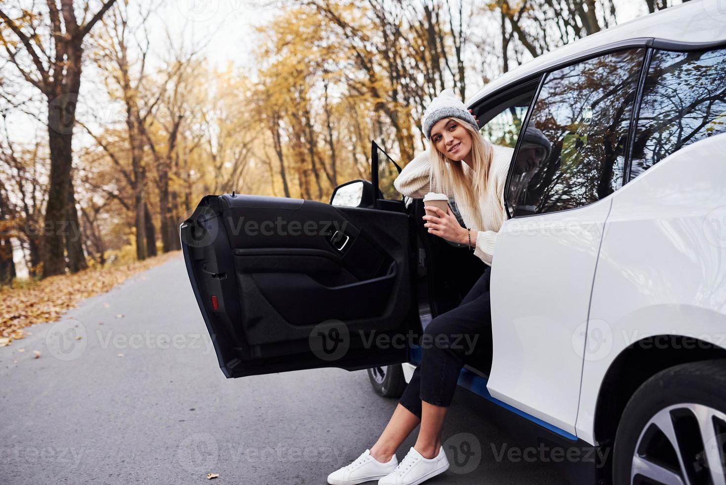 con tazza di bevanda nel mani. ragazza avere autunno viaggio di macchina. moderno marca nuovo automobile nel il foresta foto