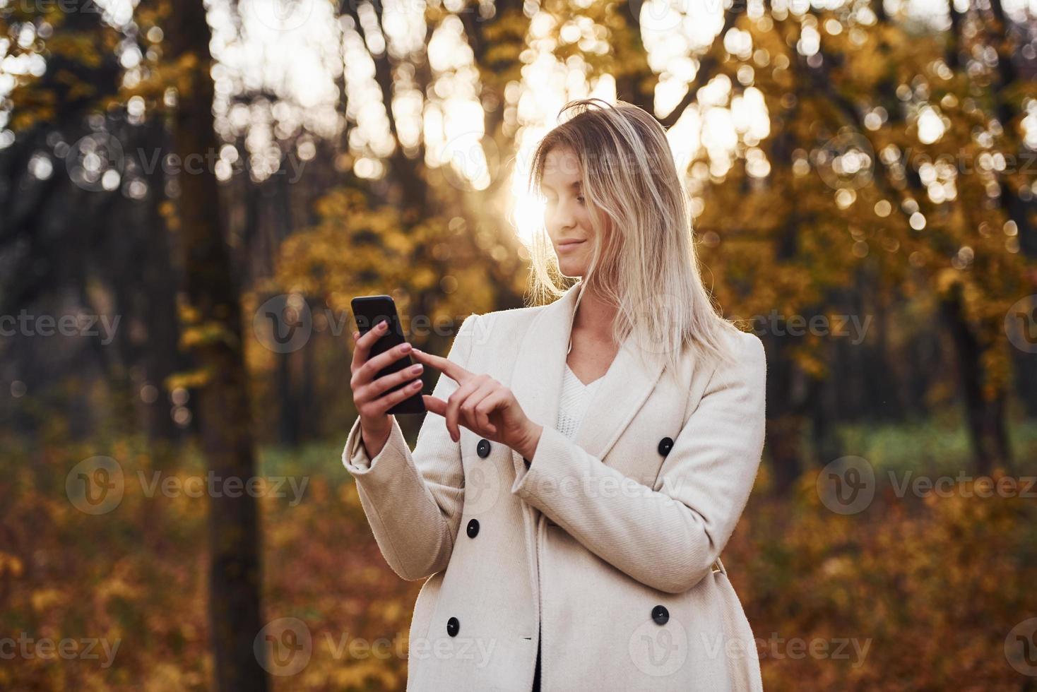 ritratto di giovane brunetta con Telefono nel mano quello è nel autunno foresta a giorno foto