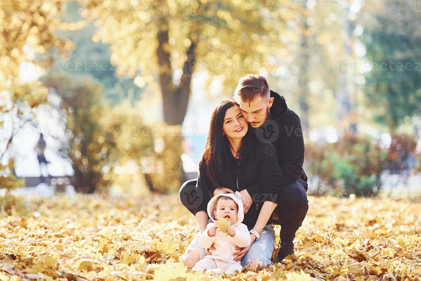 allegro famiglia si siede su il terra e avendo divertimento insieme con loro bambino nel bellissimo autunno parco foto