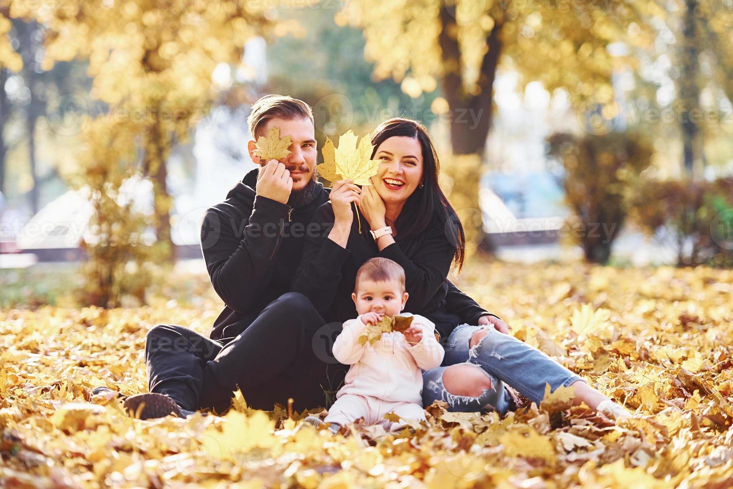 allegro famiglia si siede su il terra e avendo divertimento insieme con loro bambino nel bellissimo autunno parco foto