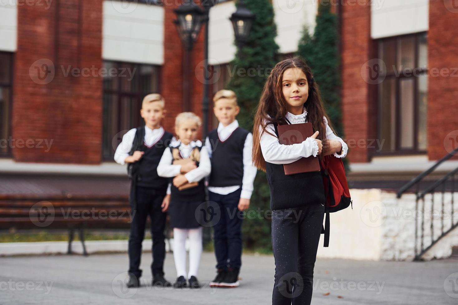 gruppo di bambini nel scuola uniforme in posa per il telecamera all'aperto insieme vicino formazione scolastica edificio foto