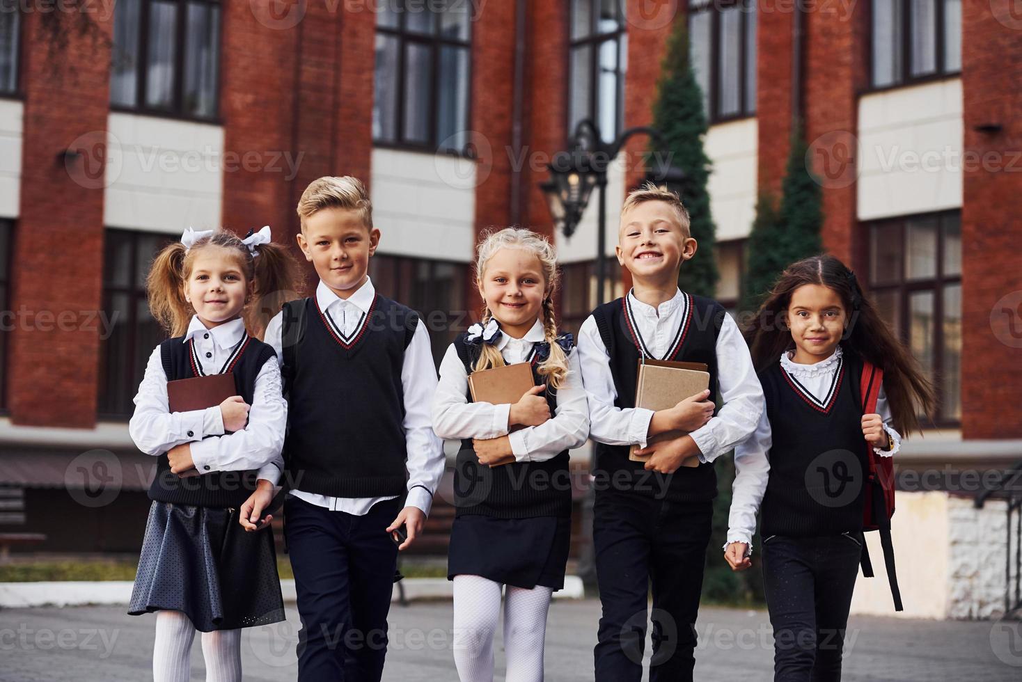 gruppo di bambini nel scuola uniforme quello è all'aperto insieme vicino formazione scolastica edificio foto