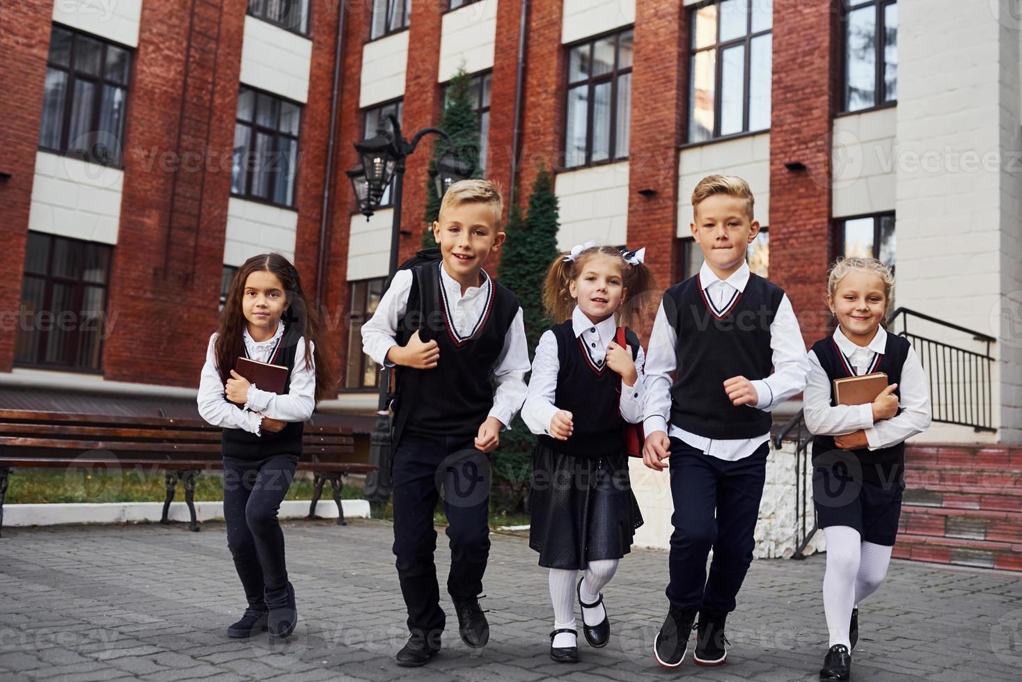 gruppo di bambini nel scuola uniforme in posa per il telecamera all'aperto insieme vicino formazione scolastica edificio foto