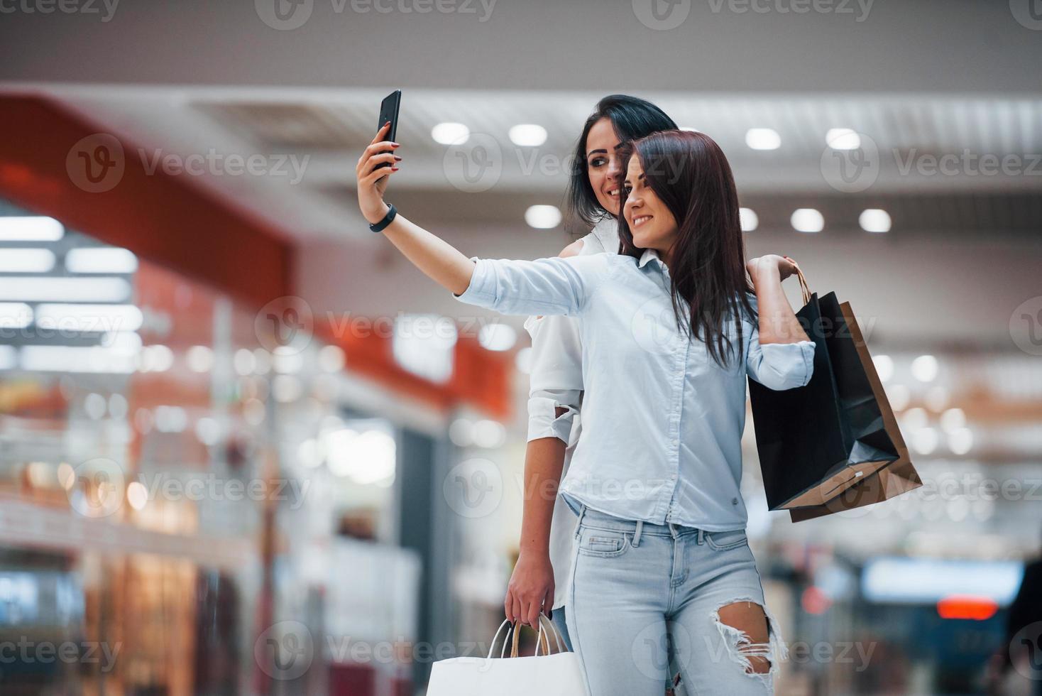 Due giovane donne avere un' shopping giorno insieme nel il supermercato e fabbricazione autoscatto foto