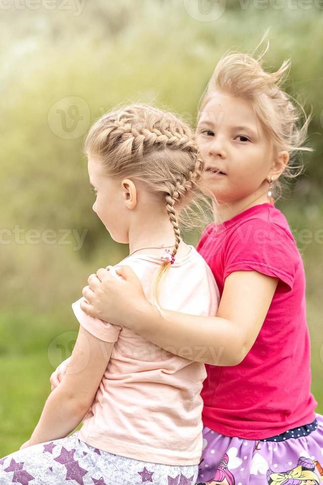 Due ragazze bambino piccolo sorelle sedersi abbracciare su il ponte nel il parco. supporto foto