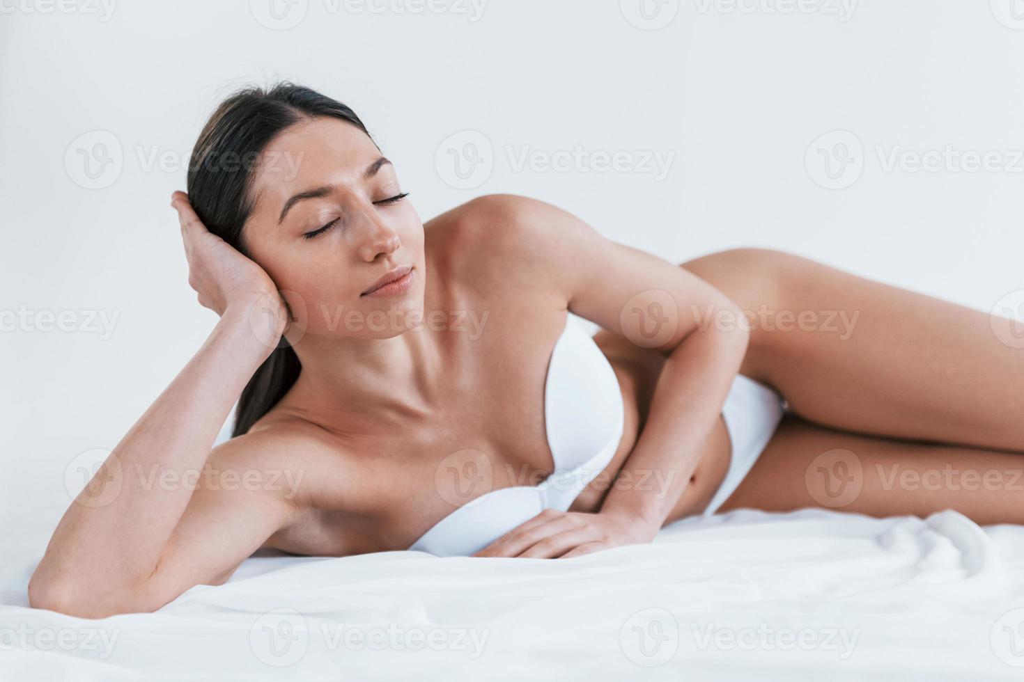 giovane donna nel biancheria intima e con simpatico corpo forma dire bugie giù nel il studio contro bianca sfondo foto