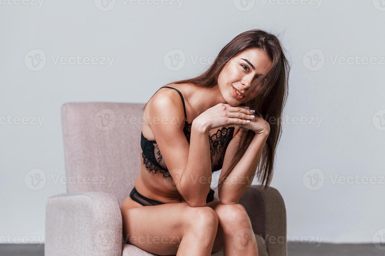 sexy donna nel nero biancheria intima seduta su il sedia nel il studio foto