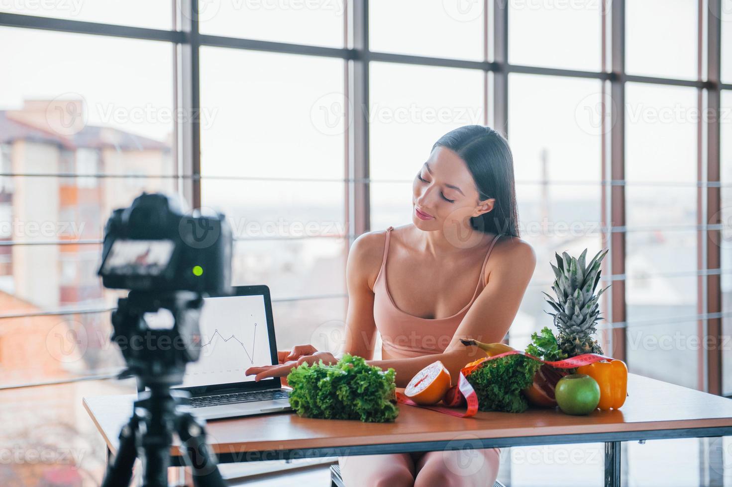 giovane fitness vlogger fare video in casa di seduta vicino tavolo con salutare cibo foto