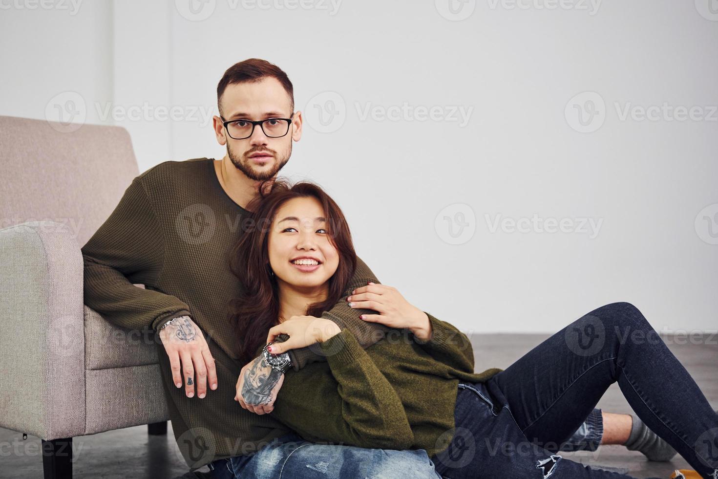 contento Multi etnico coppia nel casuale Abiti seduta insieme in casa nel il studio. caucasico tipo con asiatico fidanzata foto