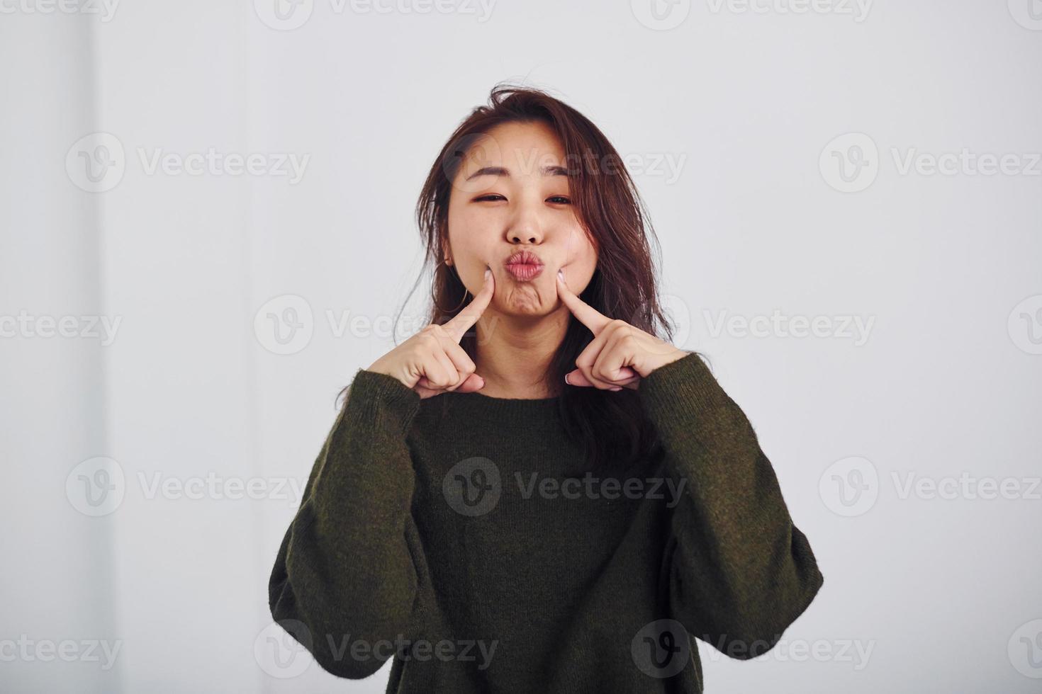 ritratto di contento asiatico giovane ragazza quello in piedi in casa nel il studio contro bianca sfondo foto