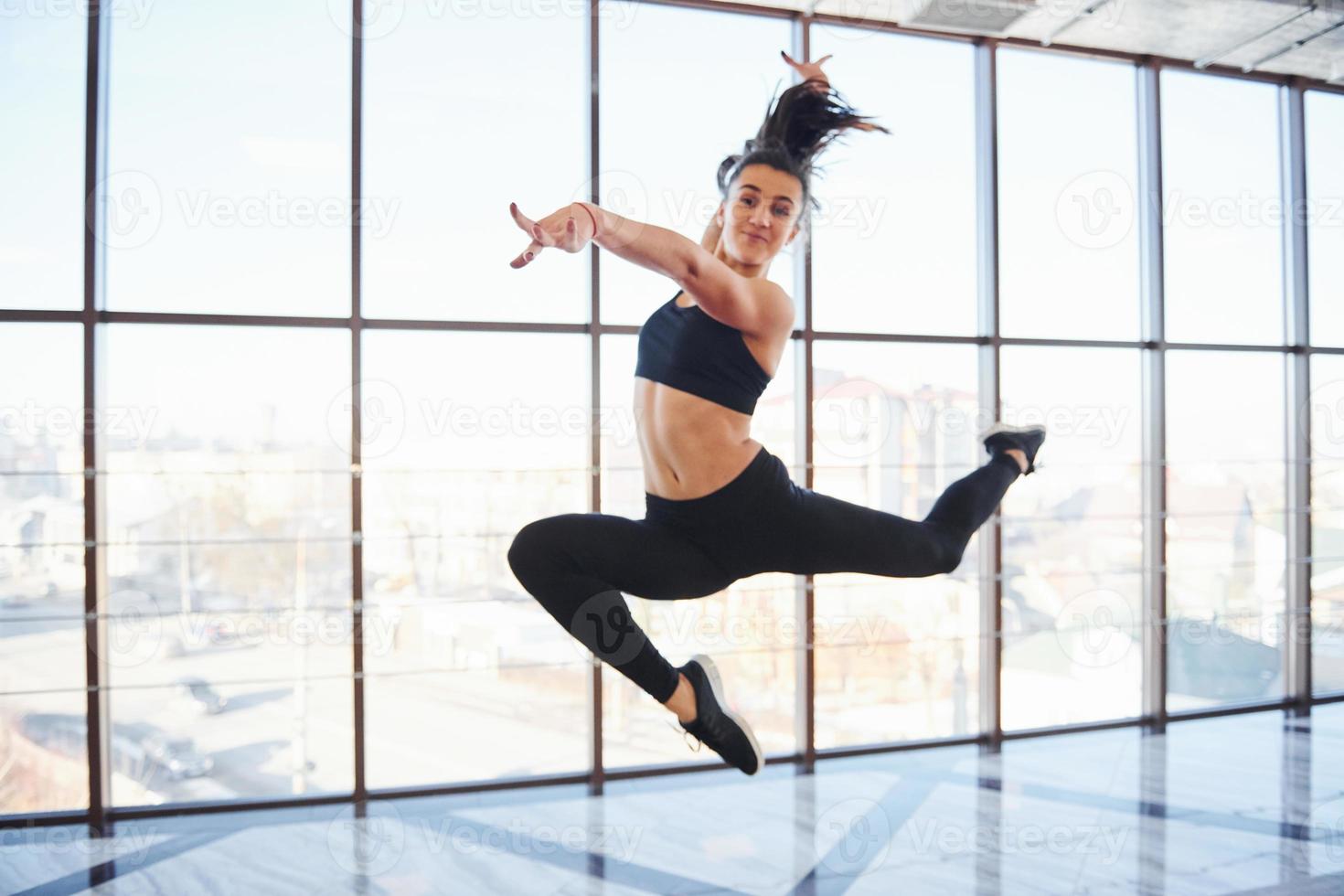 giovane sportivo donna nel abbigliamento sportivo salto e fare atletico trucchi contro finestra nel il aria foto