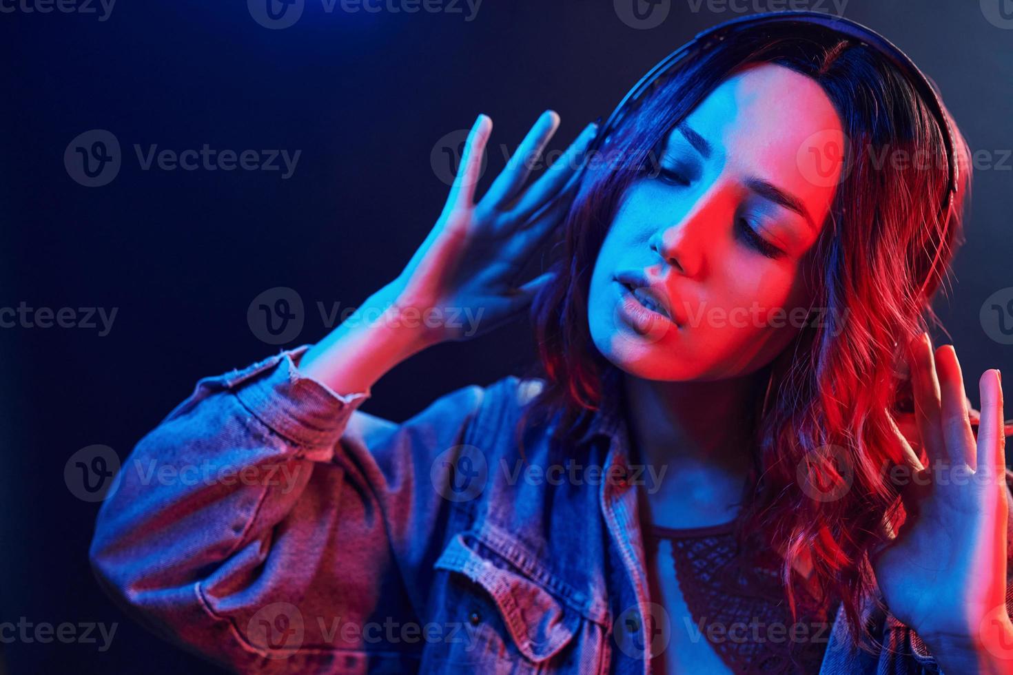 ritratto di giovane ragazza quello ascoltando per musica nel cuffie nel rosso e blu neon nel studio foto