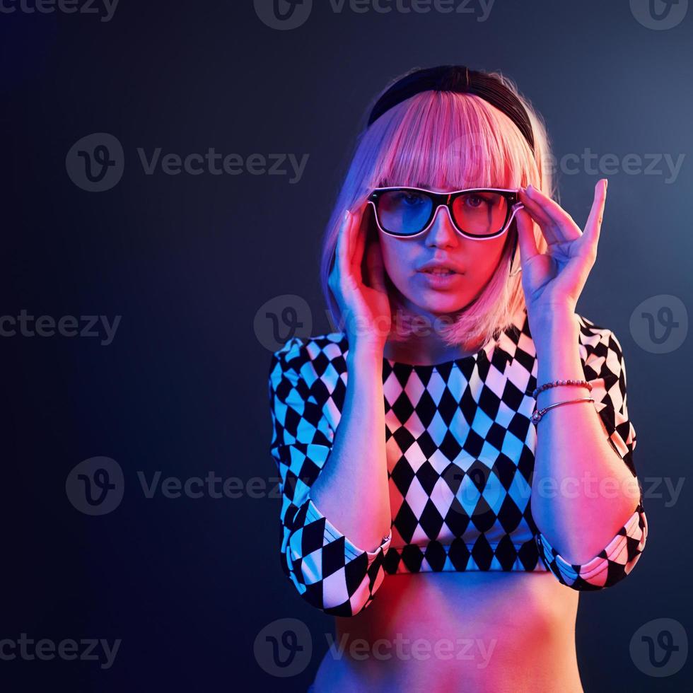 ritratto di giovane ragazza con biondo capelli nel occhiali nel rosso e blu neon nel studio foto