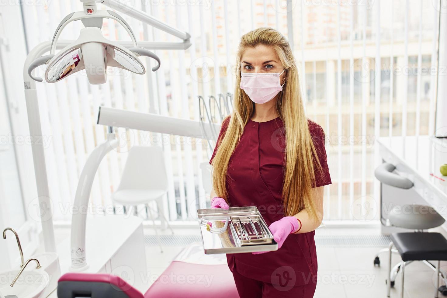giovane femmina dentista nel uniforme in piedi nel stomatologia ufficio con utensili nel mani foto
