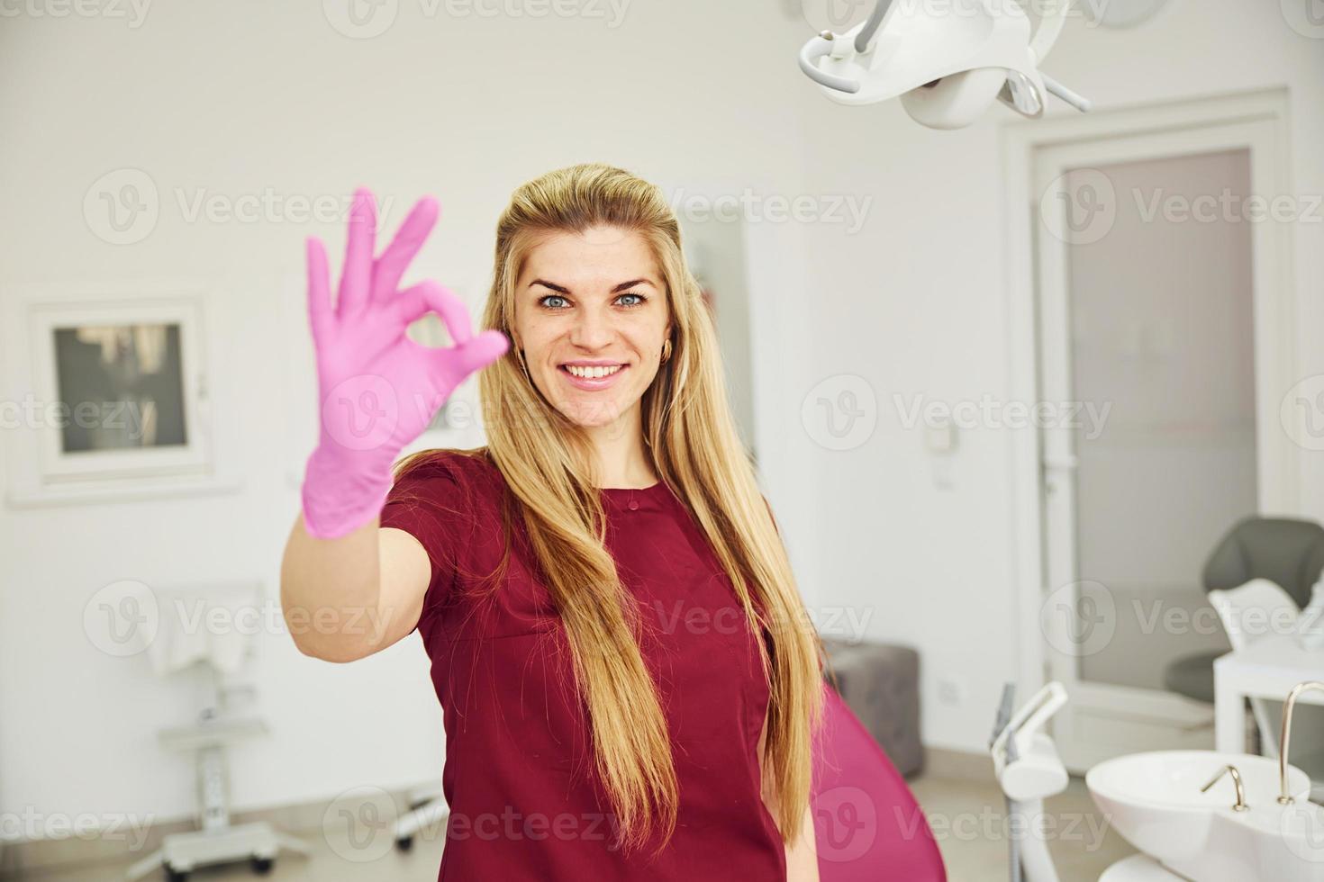 giovane femmina dentista nel uniforme in piedi nel stomatologia ufficio. Spettacoli va bene gesto foto