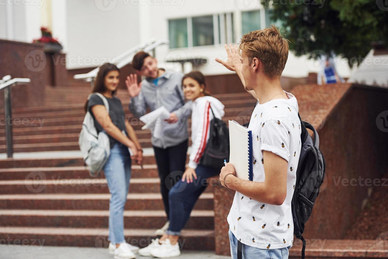 tipo avere incontrato il suo gli amici, Ciao gesto. gruppo di giovane studenti nel casuale Abiti vicino Università a giorno foto