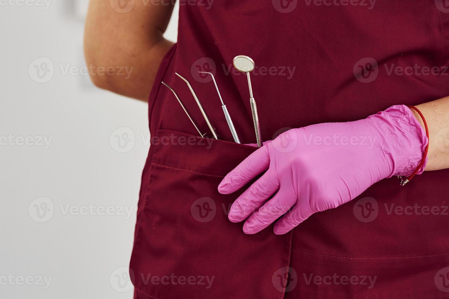 vicino su Visualizza di femmina dentista nel uniforme quello in piedi nel stomatologia ufficio con utensili nel tasca foto