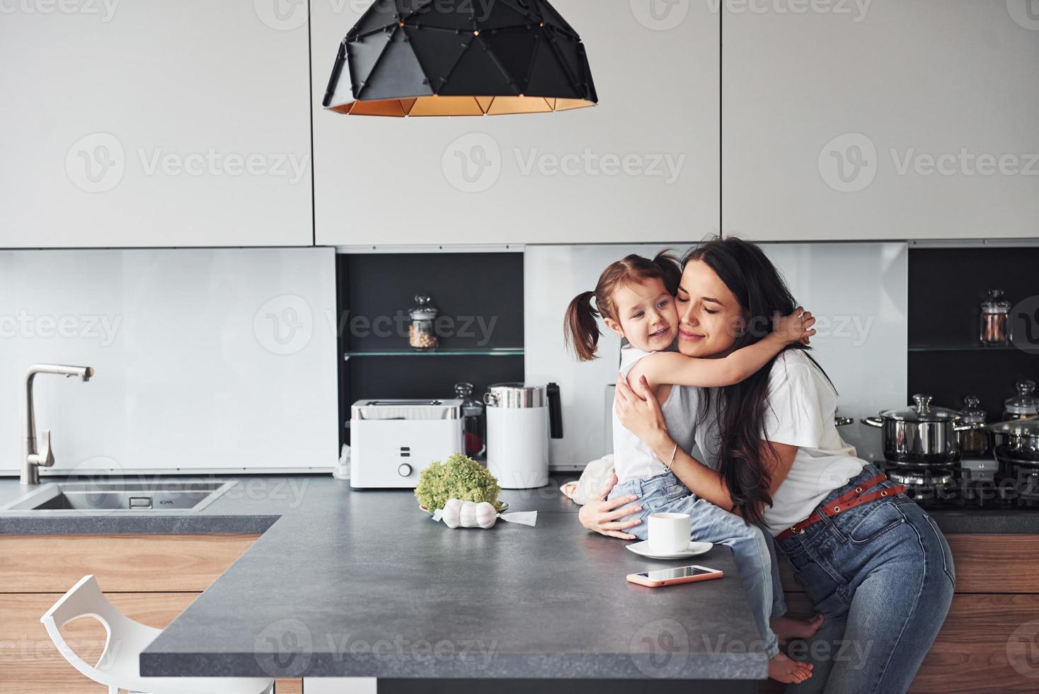 madre con sua poco figlia Abbracciare una persona ogni altro in casa nel cucina foto