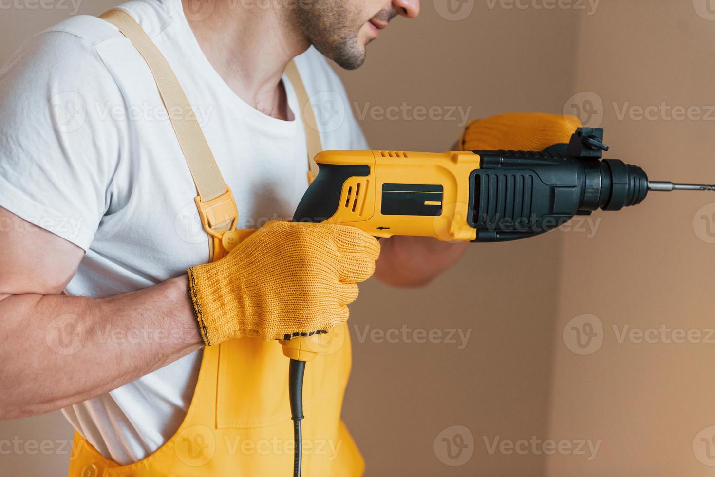 tuttofare nel giallo uniforme lavori in casa di utilizzando martello trapano. Casa rinnovamento concezione foto