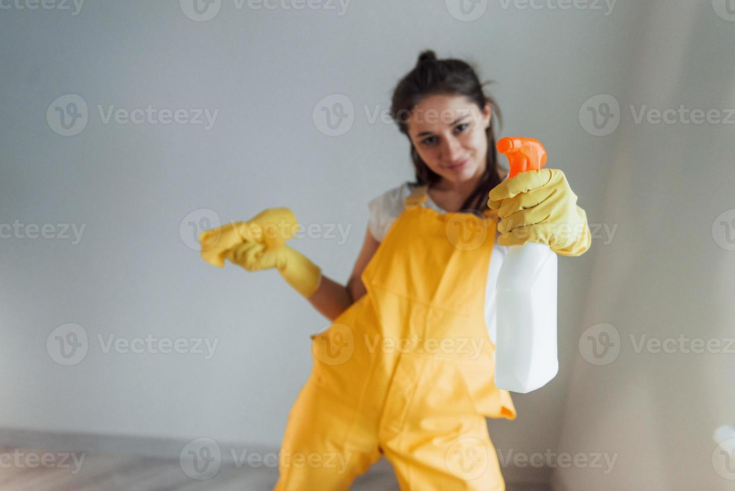 casalinga nel giallo uniforme in piedi con pulizia spray per finestre al chiuso. Casa rinnovamento concezione foto