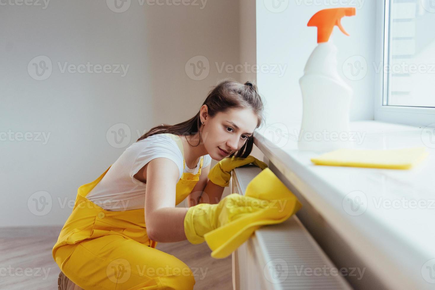 casalinga nel giallo uniforme lavori con finestra e superficie addetto alle pulizie al chiuso. Casa rinnovamento concezione foto