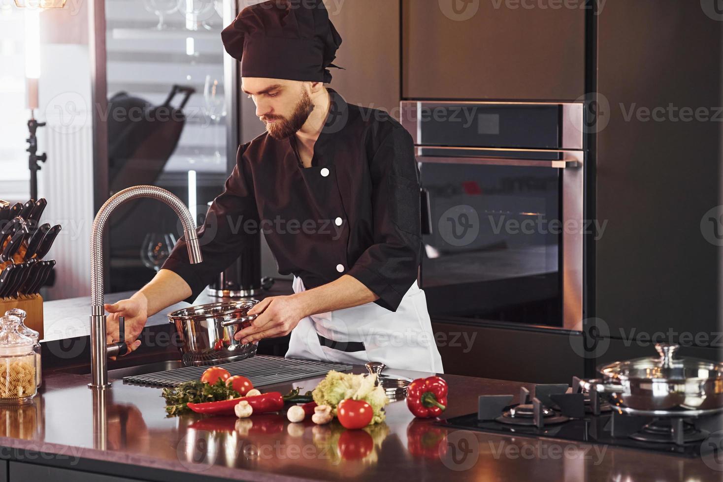 utilizzando attrezzatura. professionale giovane capocuoco cucinare nel uniforme Lavorando su il cucina con verdure foto