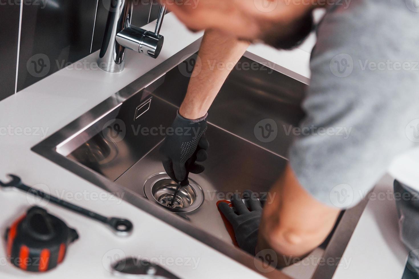giovane professionale idraulico nel grigio uniforme Lavorando su il cucina foto