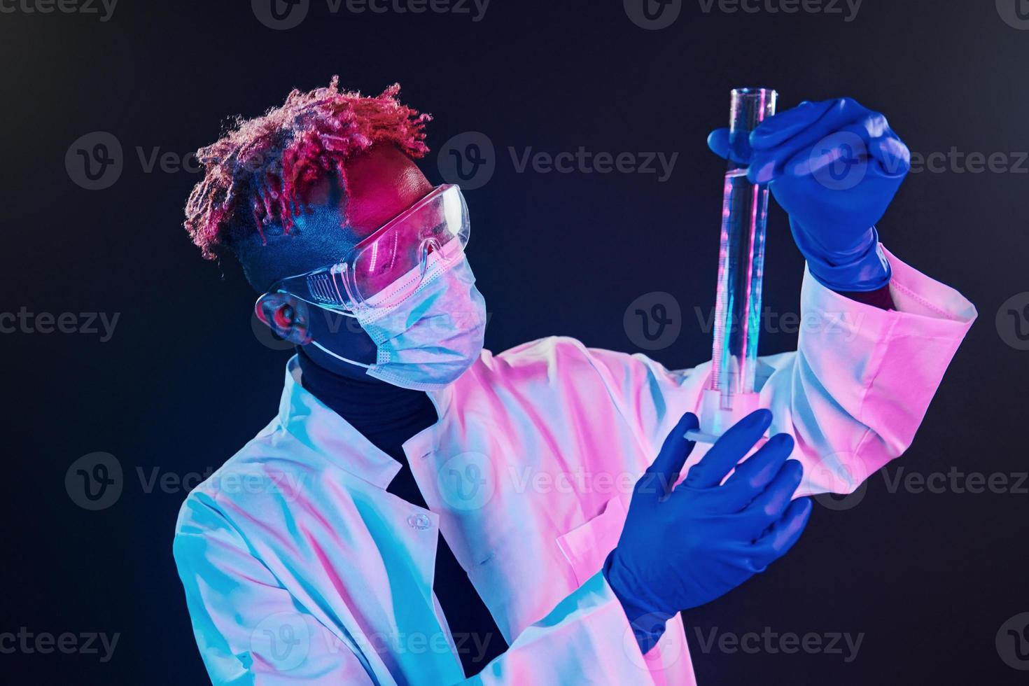inteligente scienziato nel protettivo uniforme Tenere test tubo. coronavirus concezione. futuristico neon illuminazione. giovane africano americano uomo nel il studio foto