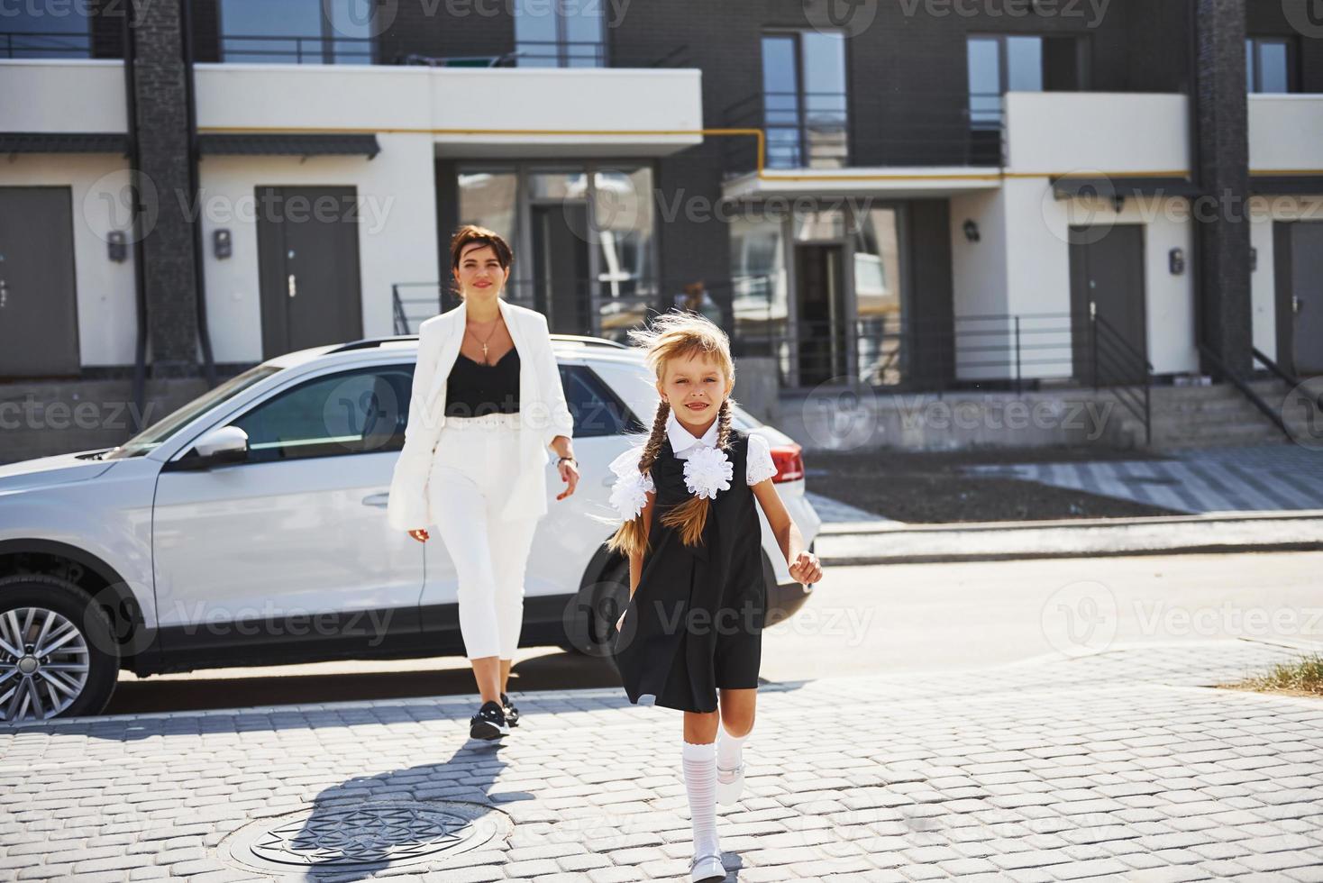 madre con figlia nel scuola uniforme all'aperto vicino bianca auto foto