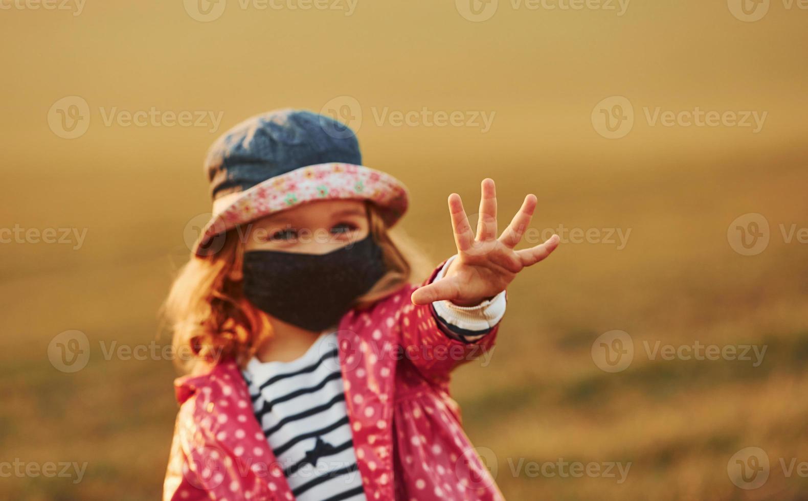 mostrando mano. ritratto di carino poco ragazza nel nero protettivo maschera quello in piedi all'aperto foto