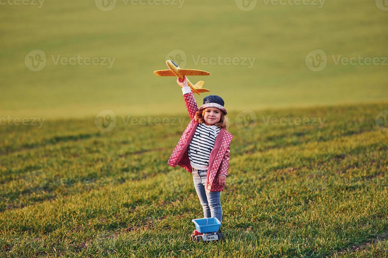 carino poco ragazza avere divertimento con giocattolo aereo su il bellissimo verde campo a soleggiato giorno foto