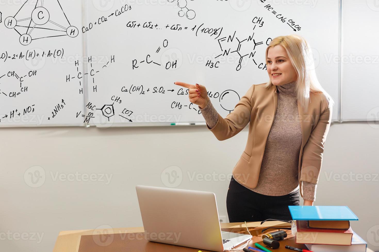 insegnante insegnamento Come per contare su lavagna nel aula. sorridente bionda donna spiegando aggiunte nel colonna nel classe. matematica insegnante spiegando aritmetica somme per elementare bambini. foto