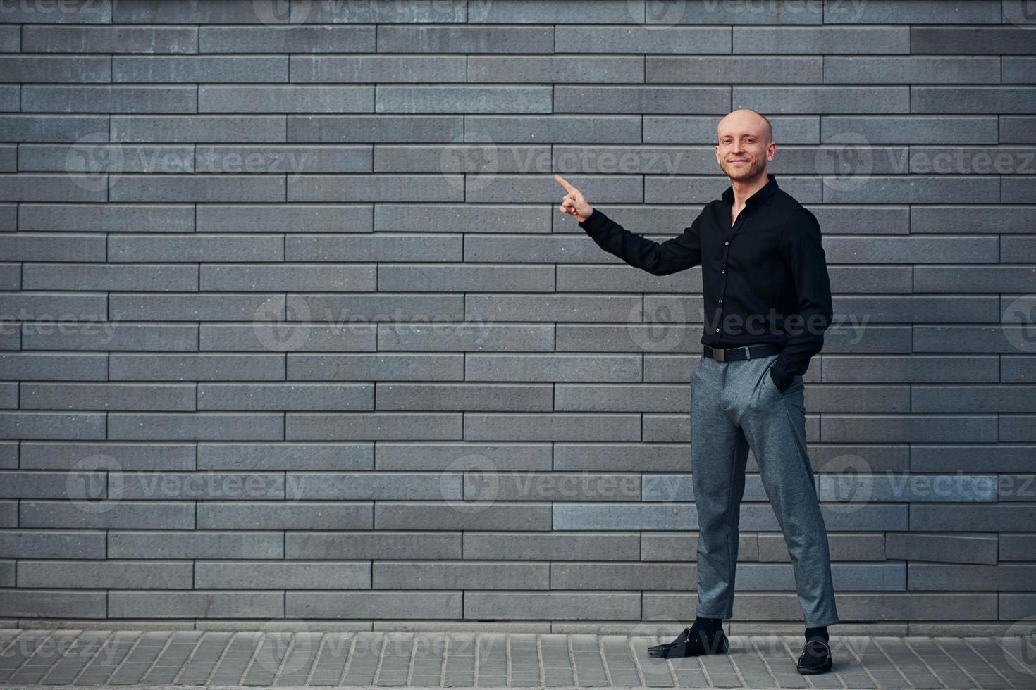 alla moda elegante uomo in piedi all'aperto contro grigio parete e Spettacoli per il sinistra di dito foto