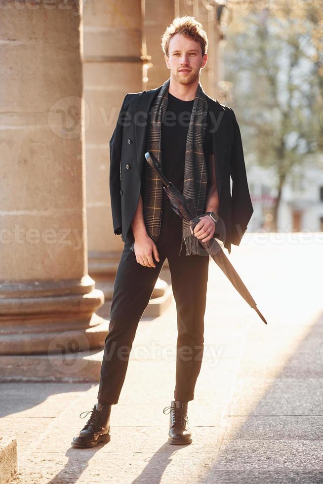 Tenere ombrello. elegante giovane uomo nel formale di classe Abiti all'aperto nel il città foto