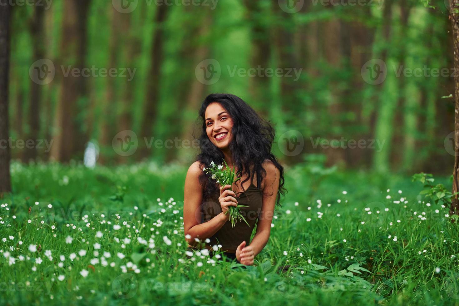 positivo brunetta nel casuale Abiti seduta nel il foresta a giorno foto