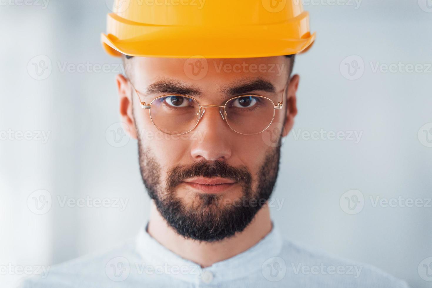 ritratto di ingegnere nel arancia protettivo difficile cappello e bicchieri quello in piedi e Lavorando in casa foto