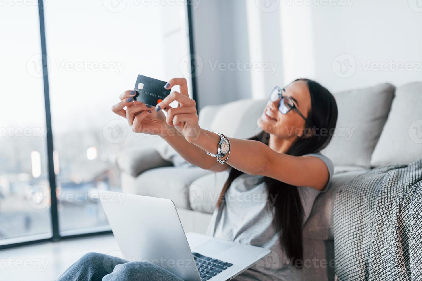 giovane bellissimo donna nel casuale Abiti seduta a casa solo con il computer portatile e credito carta foto