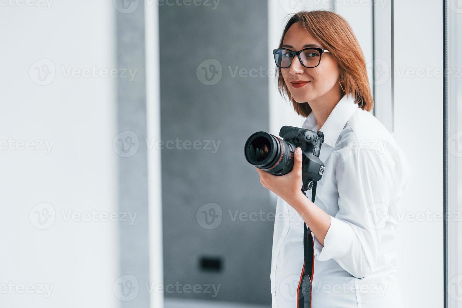 donna nel formale Abiti e con telecamera nel mano in piedi dentro di vuoto camera foto