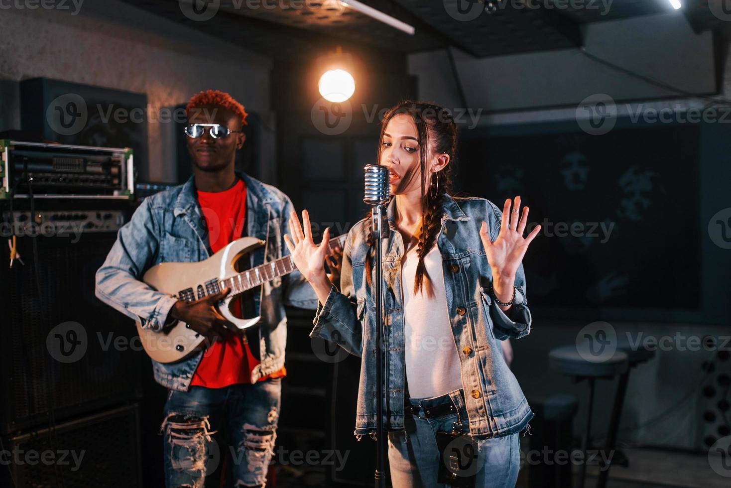 tipo giochi chitarra, ragazza canta. africano americano uomo con bianca ragazza provando nel il studio insieme foto