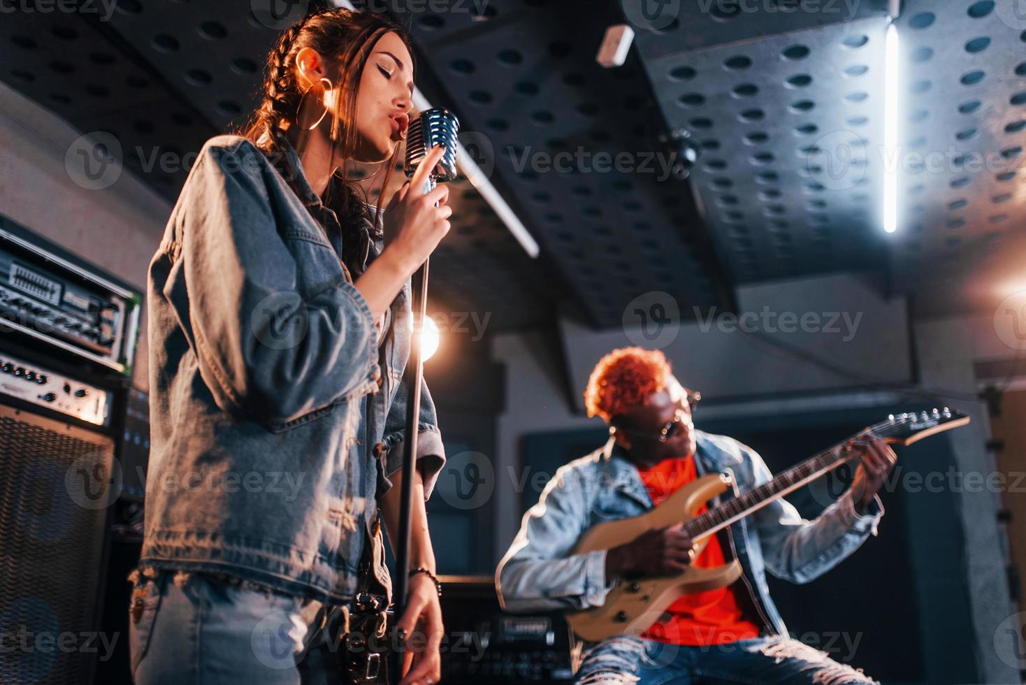 tipo giochi chitarra, ragazza canta. africano americano uomo con bianca ragazza provando nel il studio insieme foto