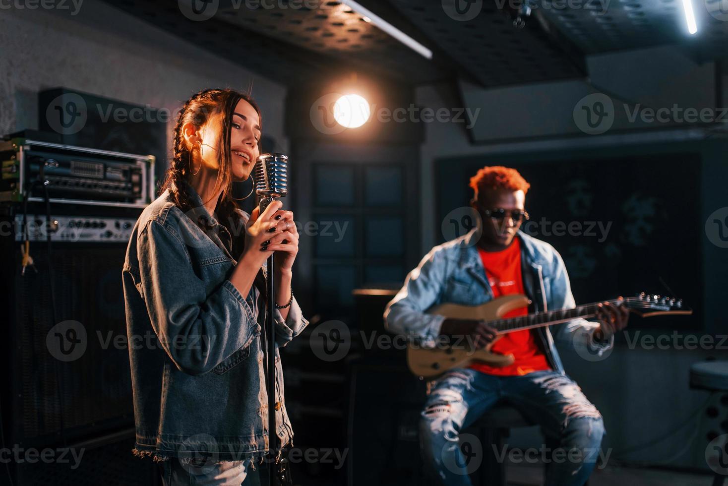 tipo giochi chitarra, ragazza canta. africano americano uomo con bianca ragazza provando nel il studio insieme foto